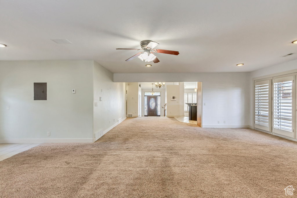 Unfurnished living room featuring light colored carpet and ceiling fan with notable chandelier