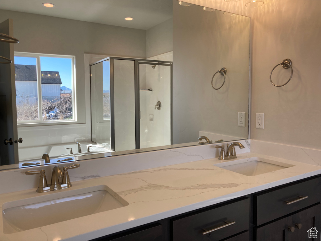 Bathroom featuring vanity with extensive cabinet space, separate shower and tub, and dual sinks