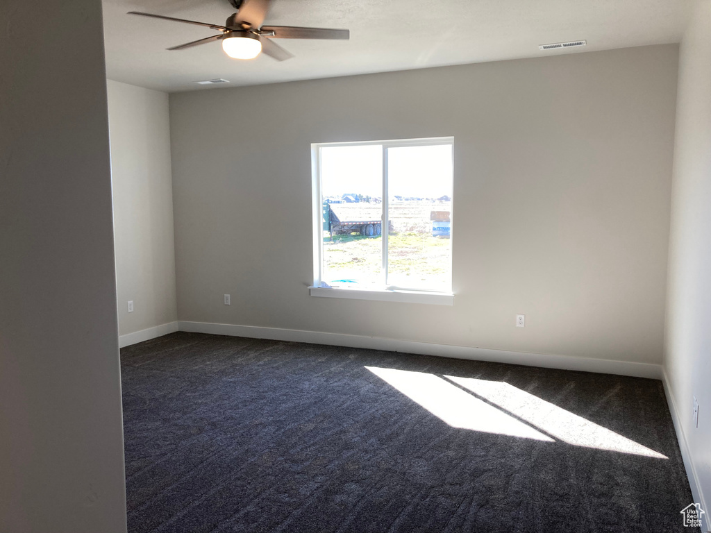 Empty room featuring dark carpet and ceiling fan