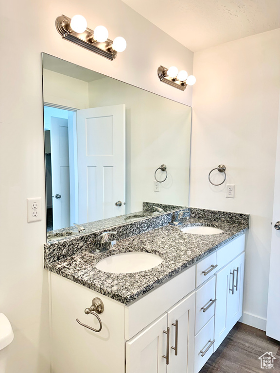 Bathroom with dual sinks, toilet, vanity with extensive cabinet space, and hardwood / wood-style floors