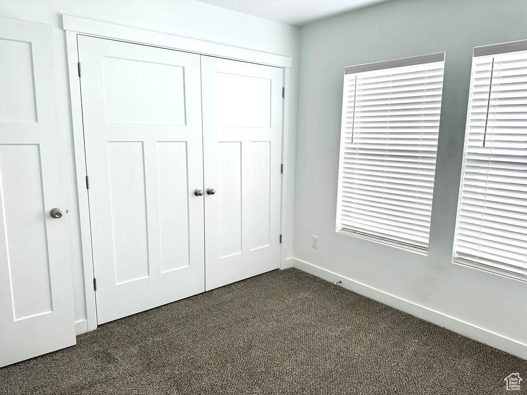 Unfurnished bedroom with a closet, multiple windows, and dark carpet