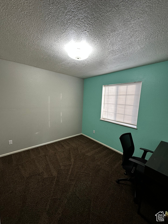 Unfurnished office featuring a textured ceiling and dark colored carpet