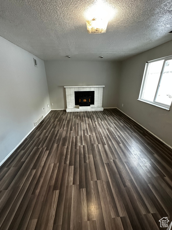 Unfurnished living room with dark hardwood / wood-style flooring, a textured ceiling, and a fireplace