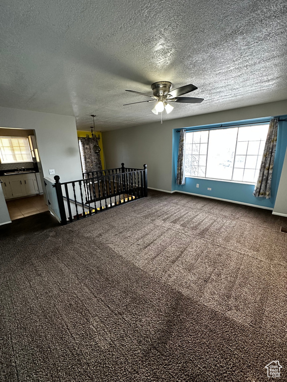 Carpeted empty room featuring a textured ceiling and ceiling fan