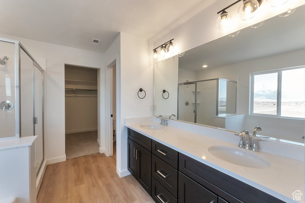 Bathroom featuring an enclosed shower, oversized vanity, dual sinks, and hardwood / wood-style flooring