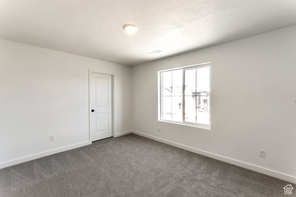 Empty room featuring dark carpet and a textured ceiling