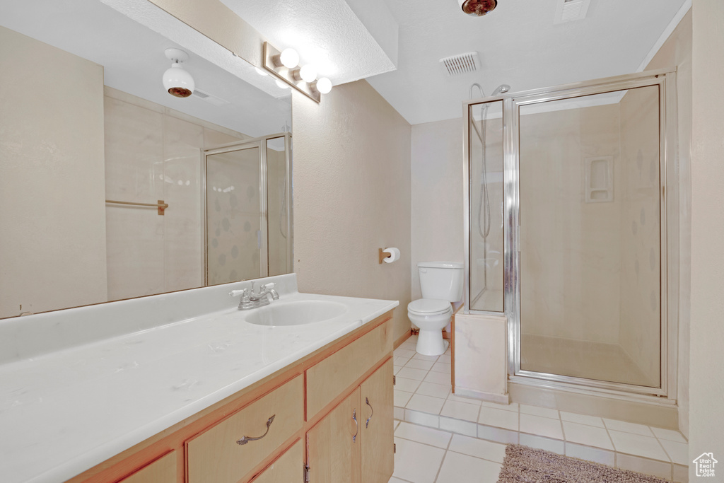Bathroom with tile floors, toilet, vanity with extensive cabinet space, and an enclosed shower