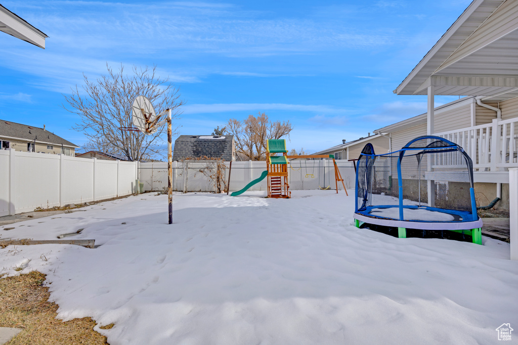 Yard covered in snow with a playground and a trampoline