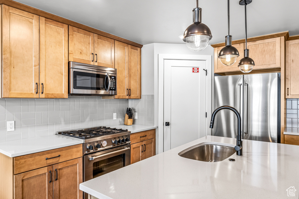 Kitchen with sink, hanging light fixtures, appliances with stainless steel finishes, and backsplash