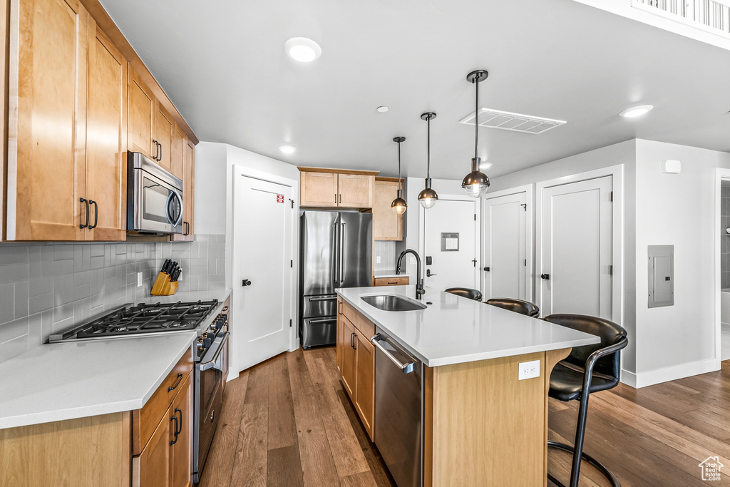 Kitchen with decorative light fixtures, hardwood / wood-style flooring, stainless steel appliances, backsplash, and a kitchen island with sink