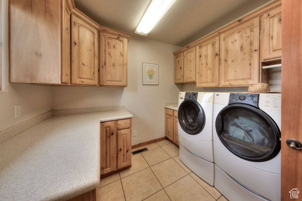 Laundry area with washing machine and clothes dryer, cabinets, and light tile floors