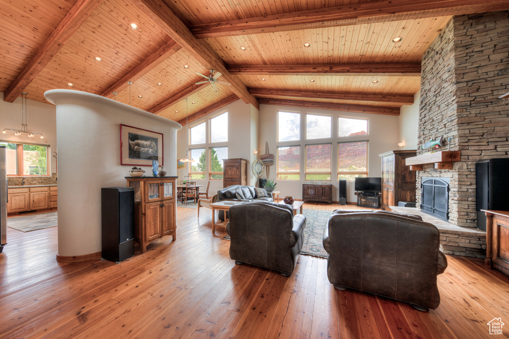 Living room featuring a stone fireplace, light wood-type flooring, high vaulted ceiling, and ceiling fan