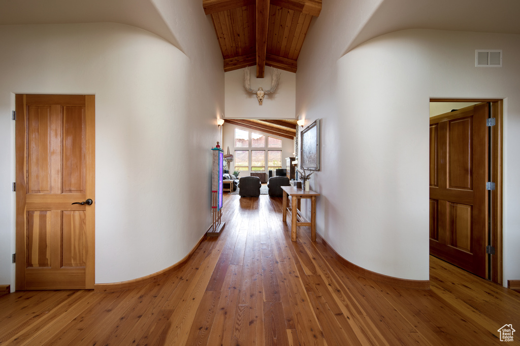 Hall with beam ceiling, light wood-type flooring, high vaulted ceiling, and wood ceiling