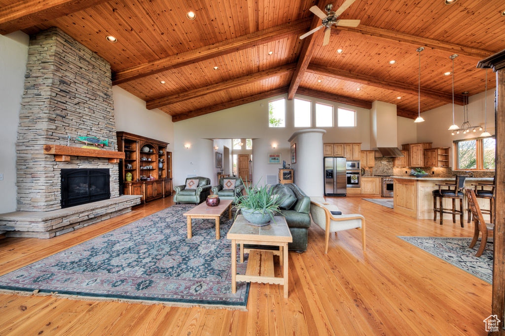 Living room featuring light hardwood / wood-style floors, ceiling fan, a stone fireplace, a wealth of natural light, and high vaulted ceiling