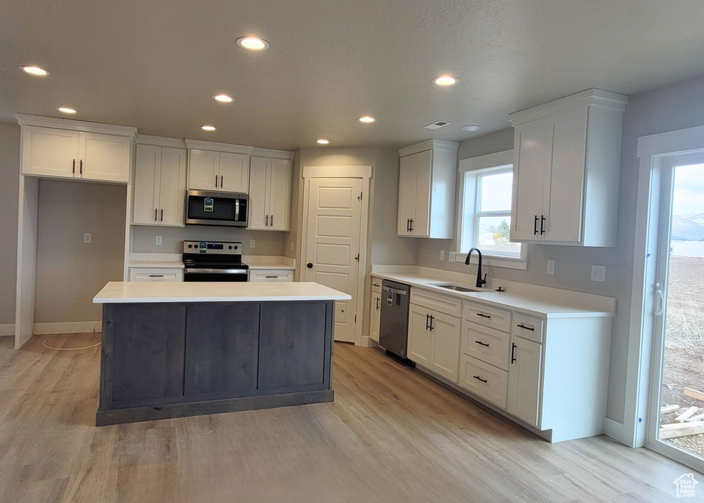 Kitchen with white cabinetry, stainless steel appliances, sink, and a center island