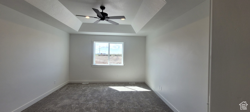 Carpeted empty room with a raised ceiling and ceiling fan