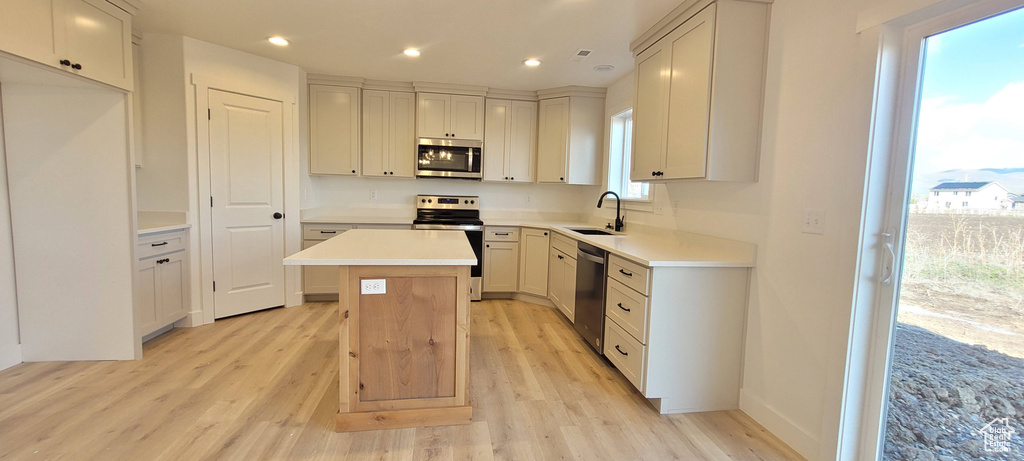 Kitchen with stainless steel appliances, a center island, white cabinets, light wood-type flooring, and sink