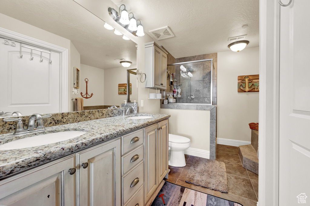 Bathroom featuring a textured ceiling, toilet, a shower with shower door, tile floors, and dual vanity