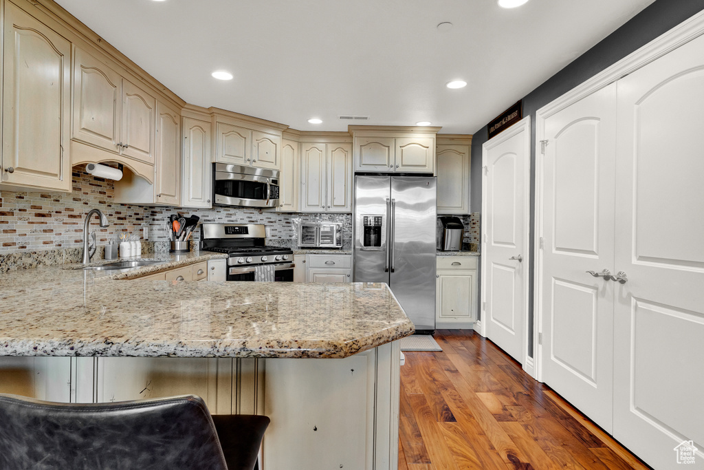 Kitchen featuring stainless steel appliances, hardwood / wood-style flooring, a breakfast bar area, backsplash, and sink