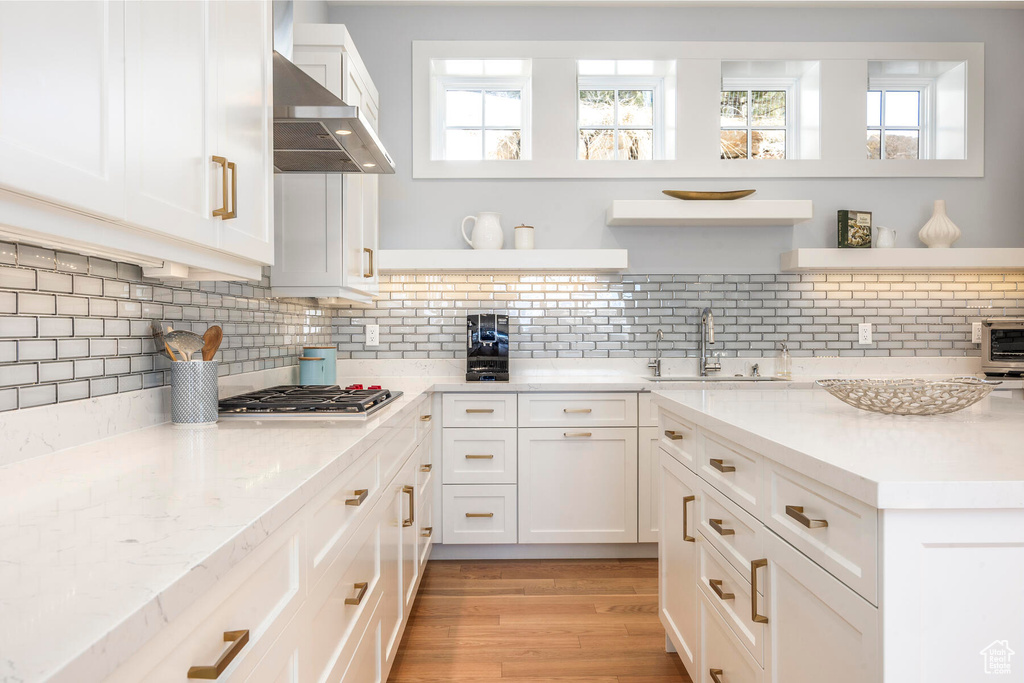 Kitchen with white cabinets, backsplash, light hardwood / wood-style flooring, wall chimney range hood, and sink
