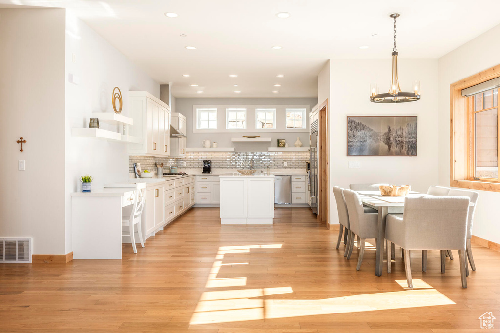 Kitchen with pendant lighting, stainless steel appliances, white cabinets, a kitchen island, and light hardwood / wood-style flooring