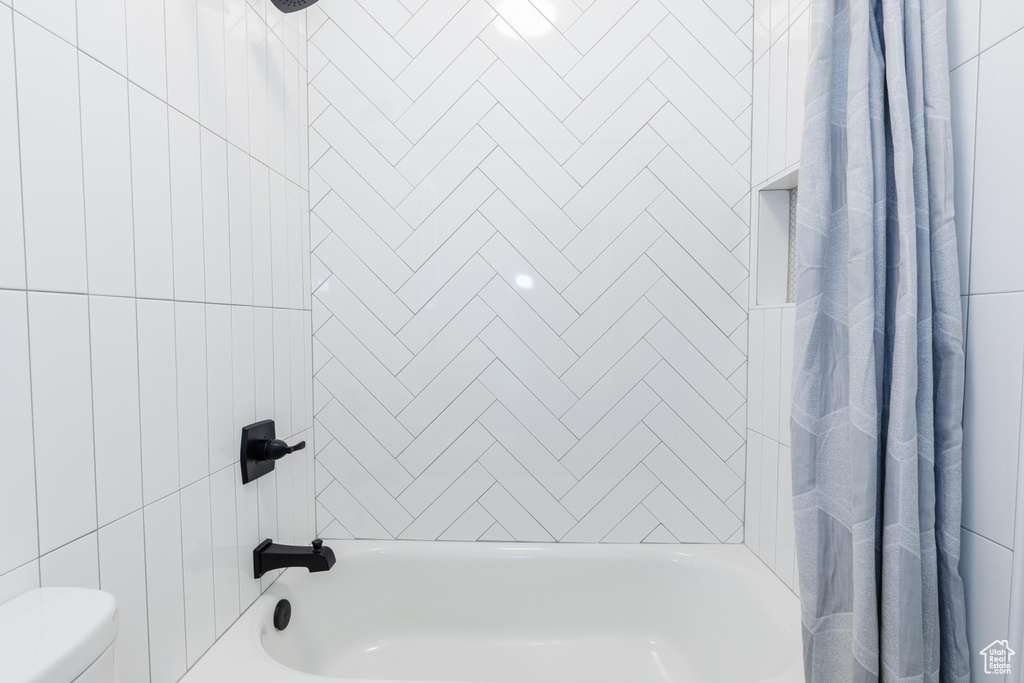 Bathroom with toilet, tile walls, and shower / bath combo with shower curtain
