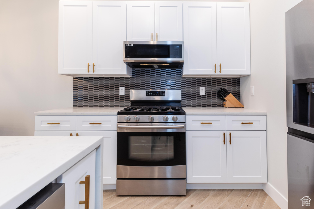 Kitchen featuring tasteful backsplash, white cabinets, light hardwood / wood-style floors, and stainless steel appliances
