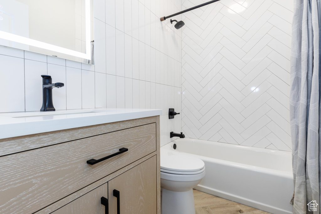 Full bathroom with toilet, vanity, tile walls, parquet flooring, and shower / bath combo
