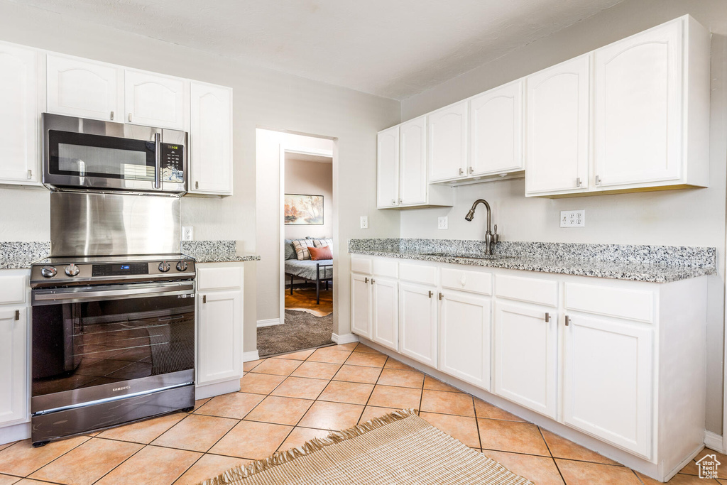 Kitchen featuring white cabinets, light stone countertops, sink, stainless steel appliances, and light tile flooring