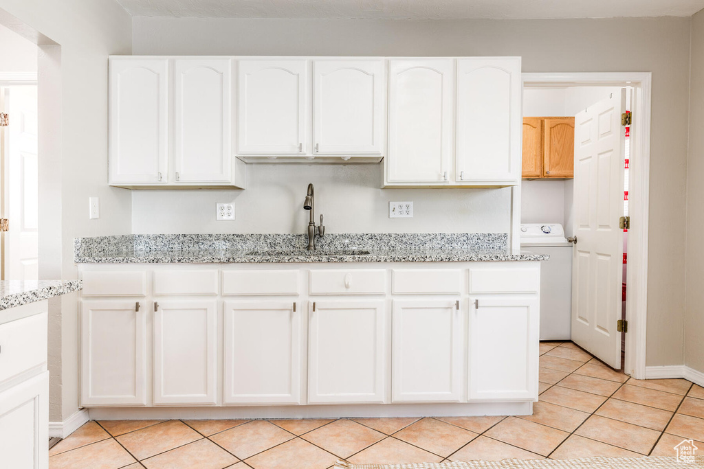 Kitchen with sink, washer / clothes dryer, light stone counters, and white cabinets