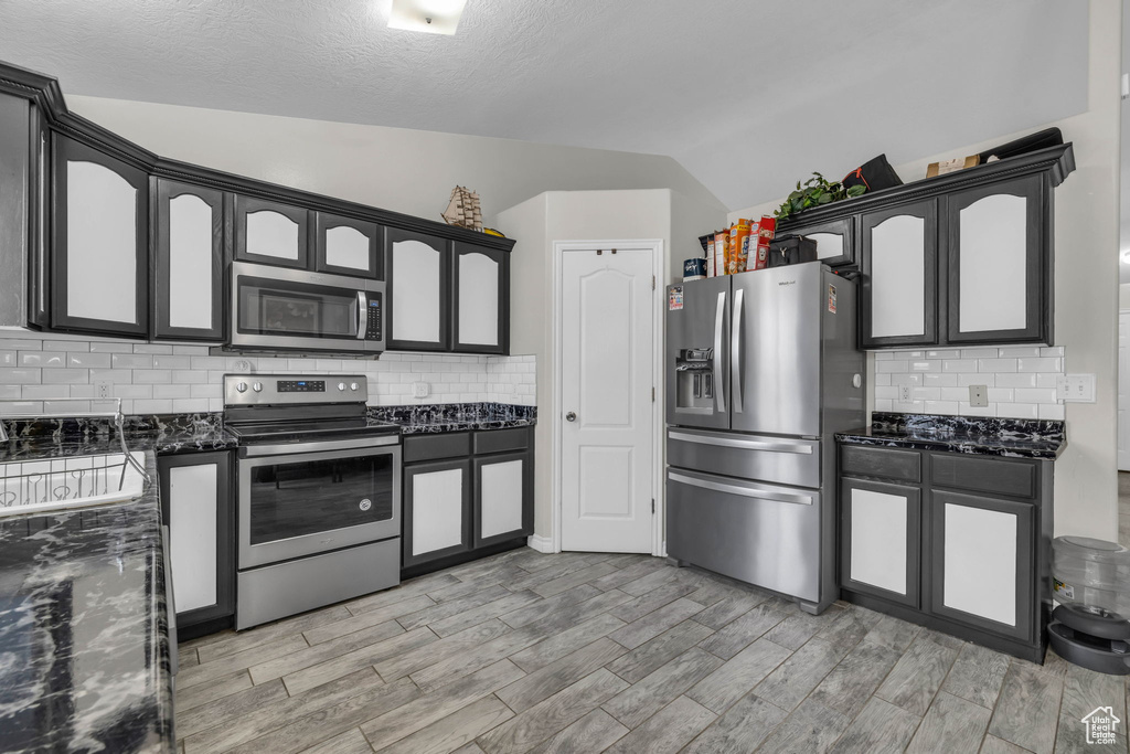 Kitchen featuring stainless steel appliances, tasteful backsplash, vaulted ceiling, and light hardwood / wood-style flooring