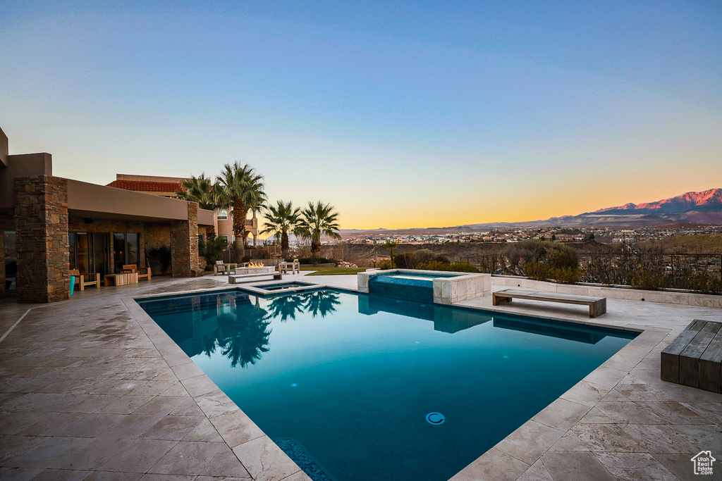 Pool at dusk featuring an in ground hot tub and a patio