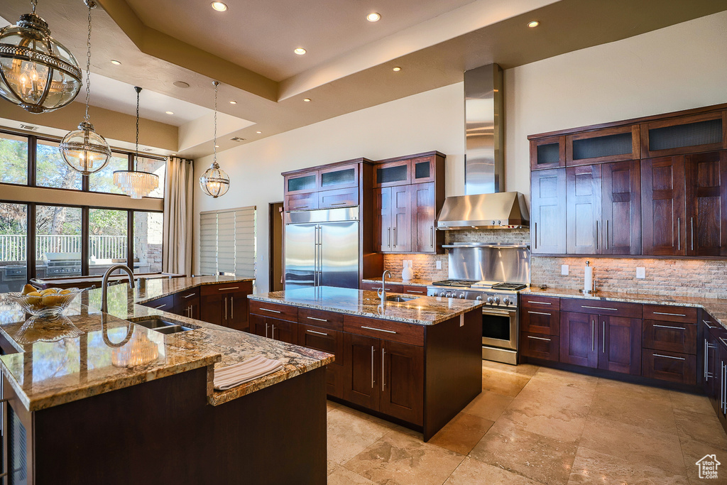 Kitchen with a center island with sink, wall chimney exhaust hood, backsplash, and premium appliances