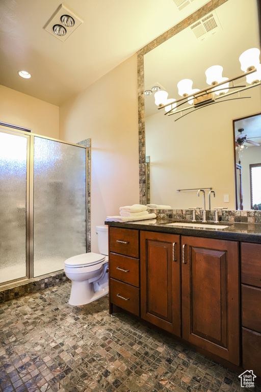 Bathroom with toilet, vanity with extensive cabinet space, ceiling fan with notable chandelier, and a shower with door