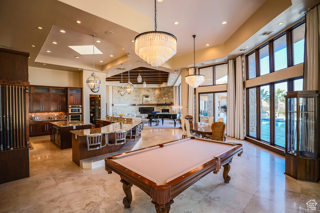 Game room with pool table, a towering ceiling, light tile flooring, and an inviting chandelier