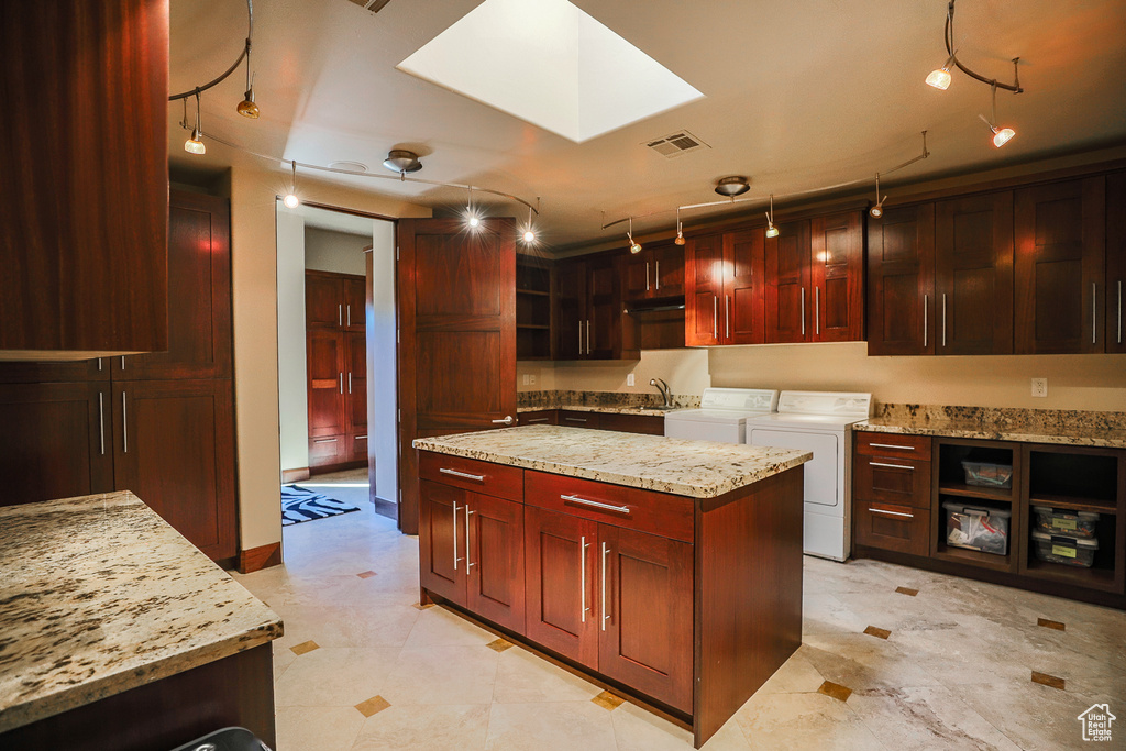Kitchen with washing machine and dryer, light tile floors, pendant lighting, light stone countertops, and a center island