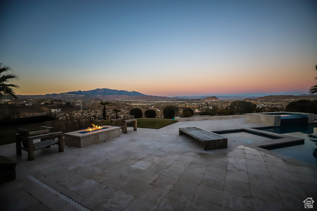 Patio terrace at dusk featuring an outdoor fire pit, a swimming pool with hot tub, and a mountain view