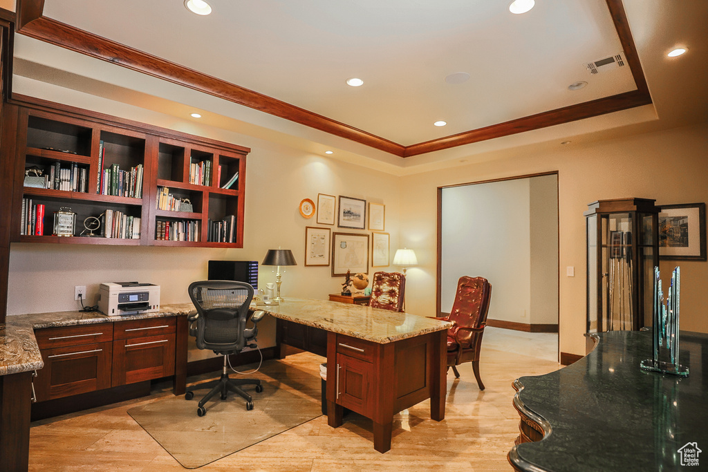 Office area with a raised ceiling, light hardwood / wood-style floors, and built in desk