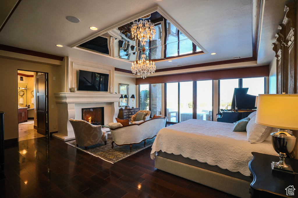 Bedroom with an inviting chandelier, a large fireplace, a raised ceiling, and dark wood-type flooring