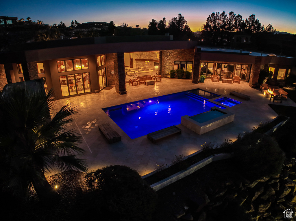 Pool at dusk with an in ground hot tub and a patio