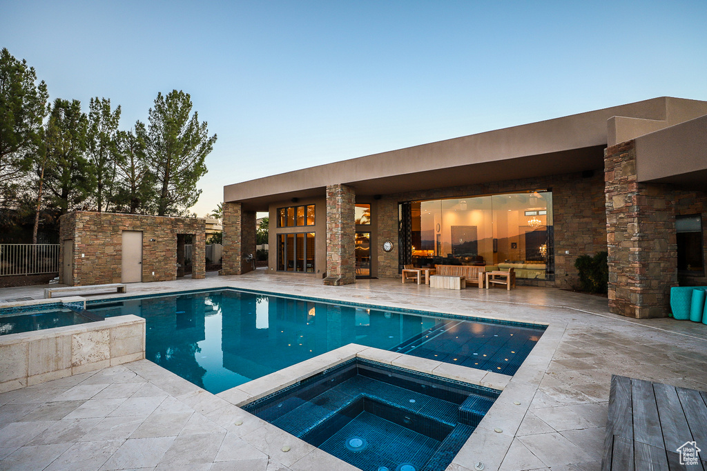 Pool at dusk featuring an in ground hot tub and a patio area