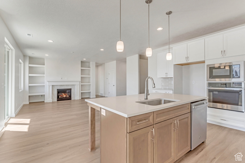 Kitchen with white cabinets, sink, appliances with stainless steel finishes, hanging light fixtures, and a center island with sink