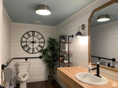 Bathroom featuring wooden walls, toilet, vanity with extensive cabinet space, and hardwood / wood-style flooring
