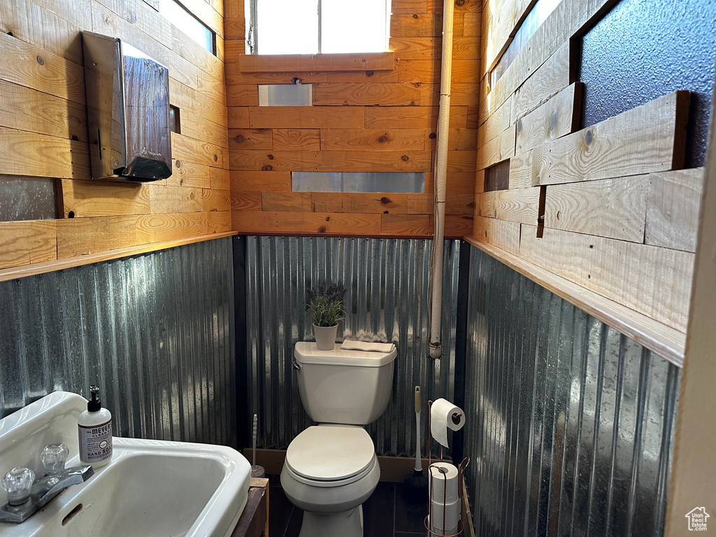 Bathroom featuring sink, toilet, and wooden walls