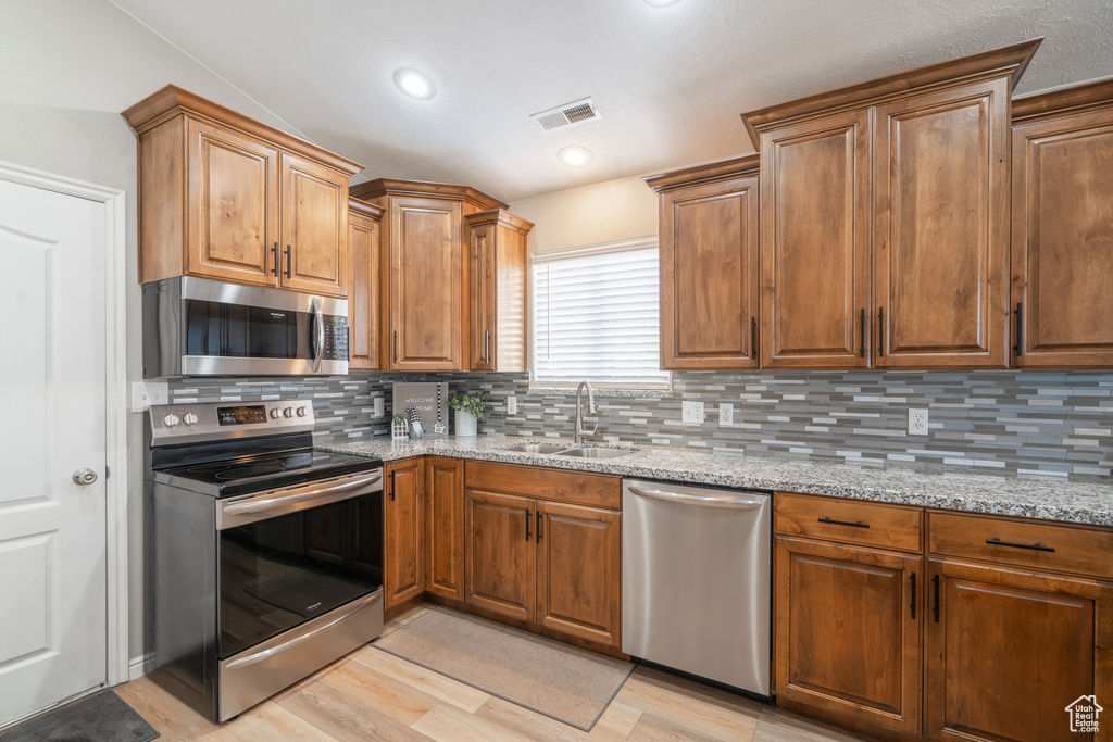 Kitchen featuring stainless steel appliances, light stone counters, backsplash, light hardwood / wood-style floors, and sink