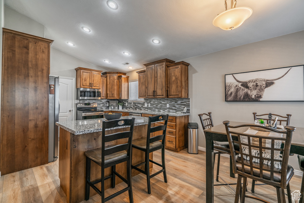 Kitchen featuring a kitchen island, appliances with stainless steel finishes, light hardwood / wood-style floors, and stone countertops