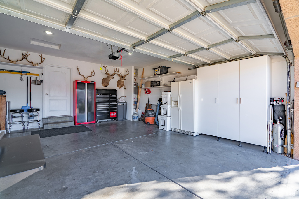 Garage featuring a garage door opener and white refrigerator with ice dispenser