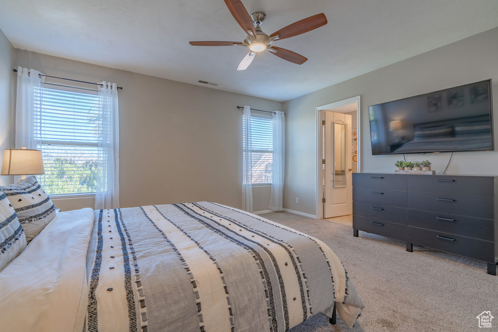 Bedroom featuring light carpet, ceiling fan, multiple windows, and ensuite bath