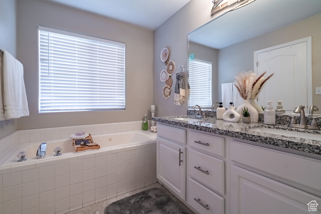 Bathroom with plenty of natural light, dual bowl vanity, and a relaxing tiled bath
