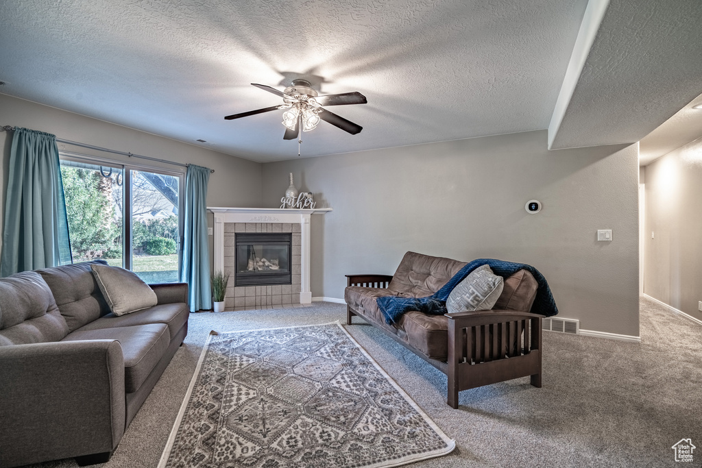 Carpeted living room featuring a fireplace, ceiling fan, and a textured ceiling
